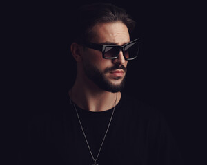 cool fashion man with beard wearing fashion sunglasses and looking to side