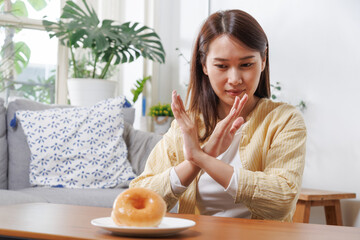 Asian female refusing the donut plate that is a mixture of trans fat. diet woman push out unhealthy food. Healthy lifestyle concept. - obrazy, fototapety, plakaty