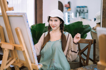 Creative painter painting in an art studio. Artistic young woman working on a new painting. Cheerful young artist looking at the camera while holding a paintbrush.