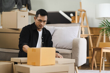 Young man carrying packed cardboard boxes with personal belongings to unfurnished cozy living room during move-in relocation day to new apartment.