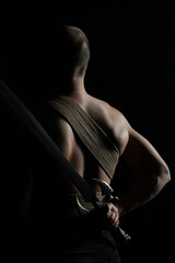 A man photographed in low key with a sword behind his back. Tied with jute rope, wrapped.