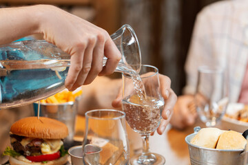 food, leisure and people concept - close up of male hands having dinner at restaurant and pouring water from jug to glass