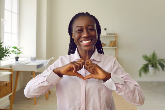 Happy Business Woman Shows Her Love And Gratitude. Video Call Headshot View Thankful African American Lady In Shirt Sitting In Home Office, Looking At Camera, Smiling, Making Heart Shape With Hands