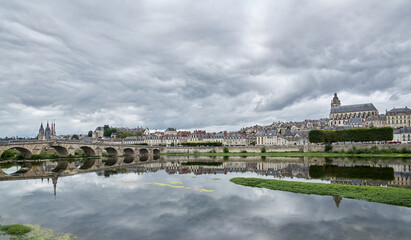 Skyline of a town with its cathedral, a river and the reflection of the bridge and the town on the waters of the river with a gray sky with many clouds
