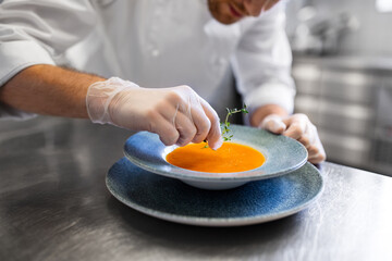 food cooking, profession and people concept - close up of male chef cook serving plate of pumpkin cream soup at restaurant kitchen
