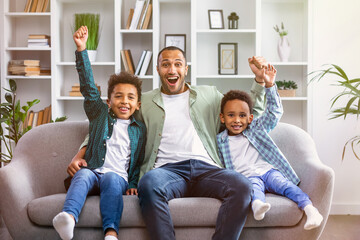 Joyful family father ans sons raising arms in triumph and celebrating incredible victory while...