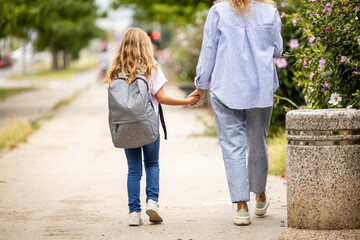 Mother and daughter holding hands together while walking towards school.