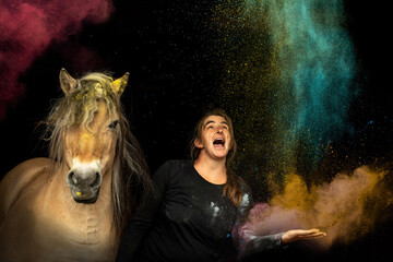 A woman and her horse covered in colorful powder on black background