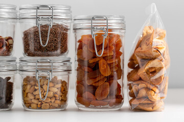 food storage, healthy eating and diet concept - close up of jars with dried fruits, seeds and nuts on table - obrazy, fototapety, plakaty