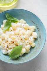 Potato gnocchi served with cheese sauce and fresh basil in a turquoise bowl, vertical shot, close-up