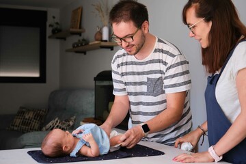 Caucasian parents changing their one month daughter diaper at home. Baby girl care.