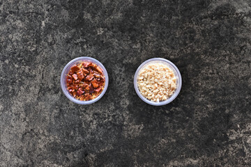 Pieces of dried spicy chili peppers and ground peanuts. Plastic boxes. Spices for flavoring food on a dark background