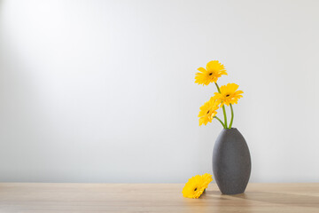 yellow gerbera in  vase on wooden shelf