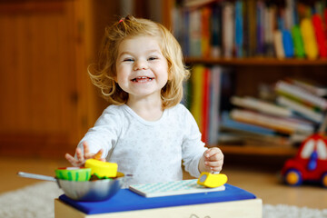 Cute little toddler girl playing at home with eco wooden toys. Happy healthy excited child cutting...