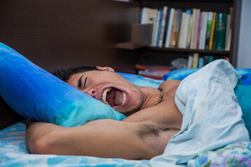 A man laying in bed with his mouth open, screaming because of a nightmare - obrazy, fototapety, plakaty