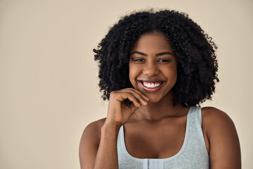 Happy young adult African American woman beauty female model, pretty 20s lady with curly hair beautiful face healthy skin looking at camera isolated at beige background. Aesthetic close up portrait.