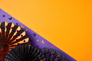 Halloween holiday flat lay composition with festive paper fans and confetti on purple and orange background.