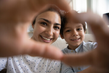 Smiling Indian mother and 5s son showing looking through heart shape gesture with fingers at camera, taking selfie, young mom with adorable boy child expressing love, happy motherhood concept
