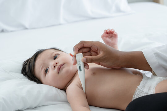 Pediatrician Doctor Measure Adorable Little 3 Month Newborn Baby Girl Temperature With A Thermometer In Armpit. Cute Infant Lying In Bed While Having Medical Check Up In Clinic. Focus On Baby