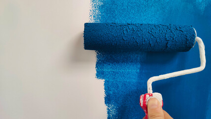 roller with blue paint on a white wall - Powered by Adobe