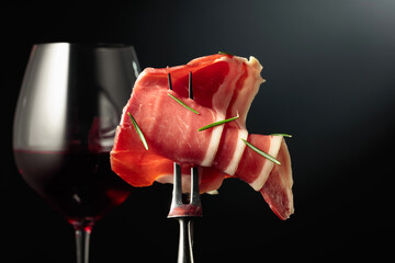 Glass of red wine and sliced prosciutto with rosemary.