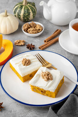 Spiced pumpkin cake with walnut and cream cheese frosting sliced into squares on a gray concrete...