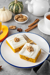 Spiced pumpkin cake with walnut and cream cheese frosting sliced into squares on a gray concrete background. Autumn dessert.