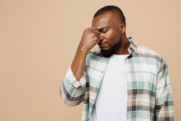 Young tired sad ill sick man of African American ethnicity he wear light shirt casual clothes keep eyes closed rub put hand on nose isolated on plain pastel beige background studio. Lifestyle concept.
