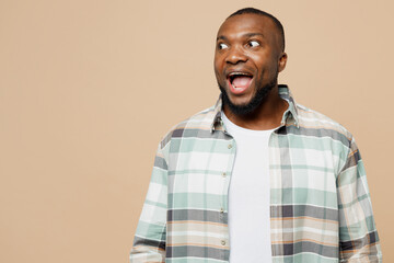 Young surpirsed shocked man of African American ethnicity he wear light shirt casual clothes look aside on workspace area isolated on plain pastel beige background studio portrait. Lifestyle concept.