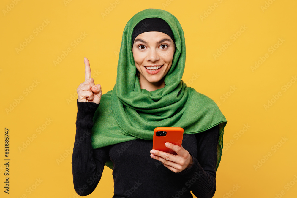 Wall mural young arabian muslim woman in green hijab abaya black clothes hold in hand use mobile cell phone poi