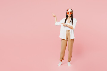 Full body young latin woman wear white shirt casual clothes sunglasses point index finger aside on area indicate on workspace area copy space mock up isolated on plain pastel light pink background.