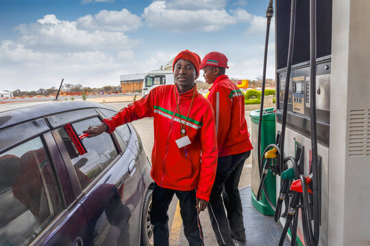 african american attendant at a petrol station washing the windows and windshield and cleaning with a blade