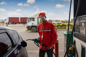 african american attendant at a petrol station holding the pump nozzle , filling a small car tank...