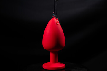 Intimate lubricant pours on a red anal plug on a black background. Copy space. 