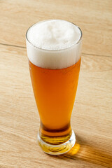 Glass of beer with foam on a wooden table.