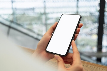 Hand holding black smartphone with blank screen for graphic display montage at shopping mall background.