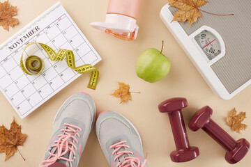 Fall season physique transformation concept. Top view photo of calendar, sneakers, floor scales, tape measure, dumbbells, water bottle, fresh apple, dry maple leaves on pastel beige background