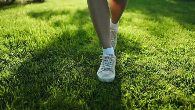 Young woman hiker legs walking on green grass at city summer park. High quality FullHD footage