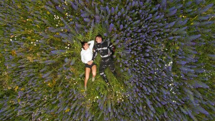 A young couple lies on a field with flowers, view from a quadcopter. The couple lies in the field. A young couple in the park sits relaxing during a hike.