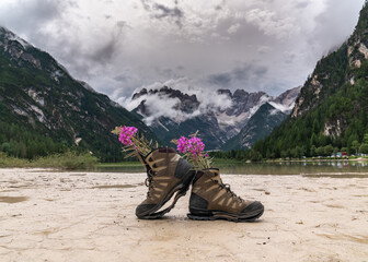 Travel and wanderlust lifestyle concept: torn hiking boots with flowers against a blue lake and beautiful mountains