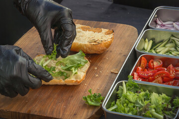 Chef puts lettuce leaves in a cut bun for making a burger or sandwich. street food - obrazy, fototapety, plakaty