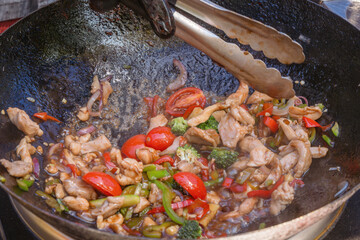Cooking Asian food from meat, seafood and vegetables in a wok on the street. Fast food