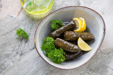 Bowl with greek dolma, fresh parsley and lemon wedges, horizontal shot on a grey granite background, high angle view