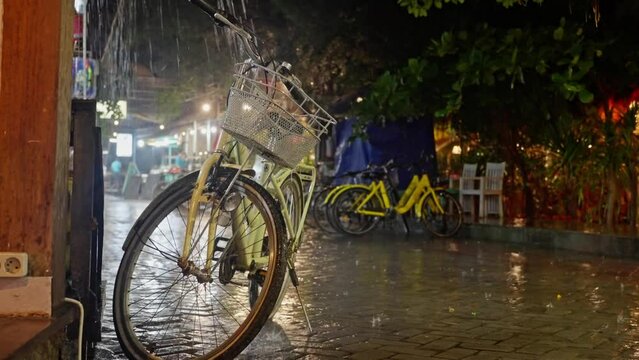 Retro yellow bicycle with bicycle bag, gets wet in the rain at night. heavy downpour in the bicycle parking lot at night, yellow Bicycle stands in the rain on the street, close-up
