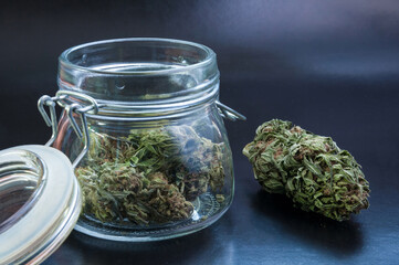 noir still life with glass mason jar full of medical cannabis buds on black background