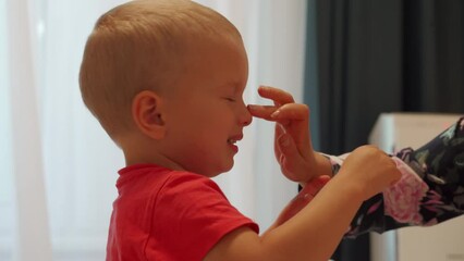 mother uses nasal aspirator baby snot sucker and nasal spray spraying saline solution in the nose of her toddler child, little boy is cold and has runny nose