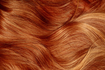 Fototapeta premium Red hair close-up as a background. Women's long orange hair. Beautifully styled wavy shiny curls. Hair coloring bright shades. Hairdressing procedures, extension.
