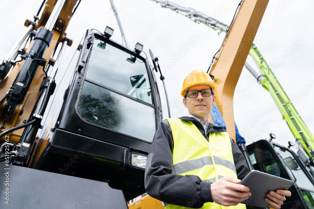 Aufkleber engineer in a helmet with a digital tablet stands next to construction excavators.