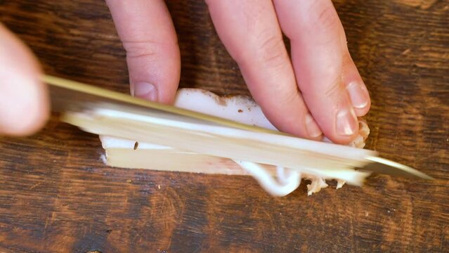 Slicing of salted pork fatback on cutting board, close-up. Ukrainian traditional food - salo