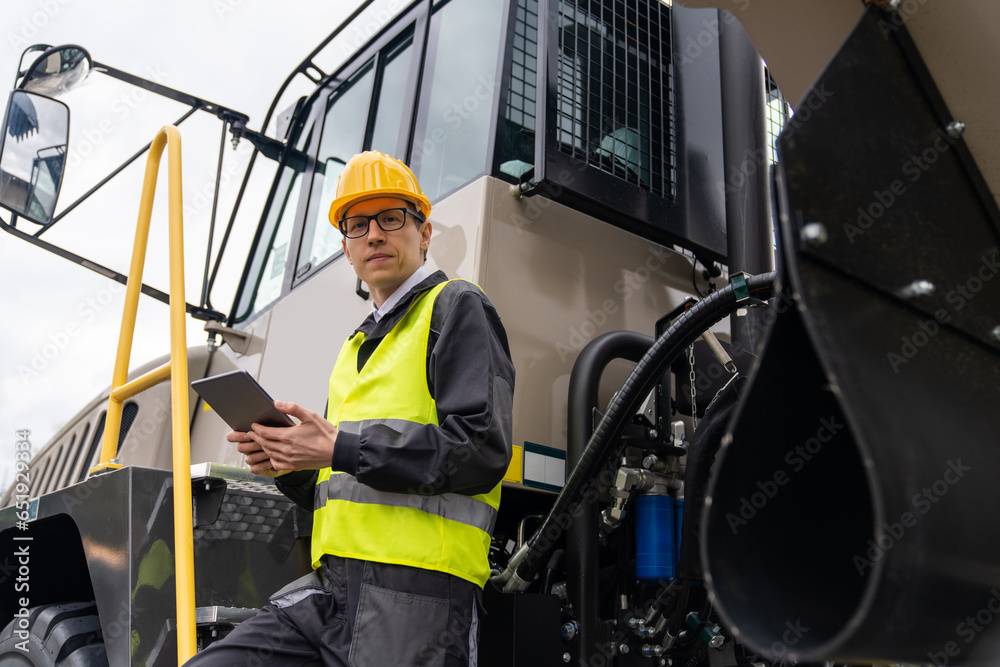 Poster engineer with tablet computer stands on the stairs to the cab of a truck.